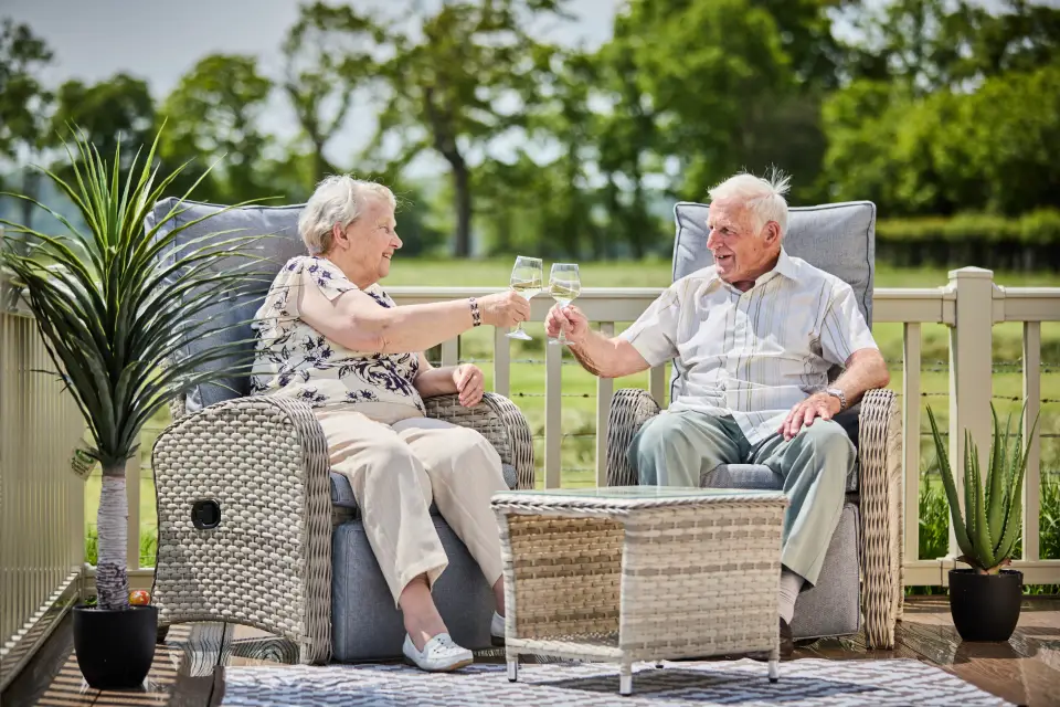 couple drinking wine on the decking of their lodge at st marys lodge park