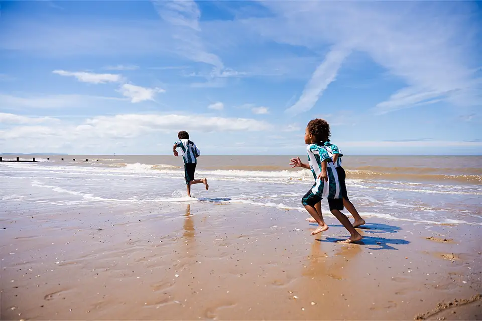 3 children running along Rhyl Beach
