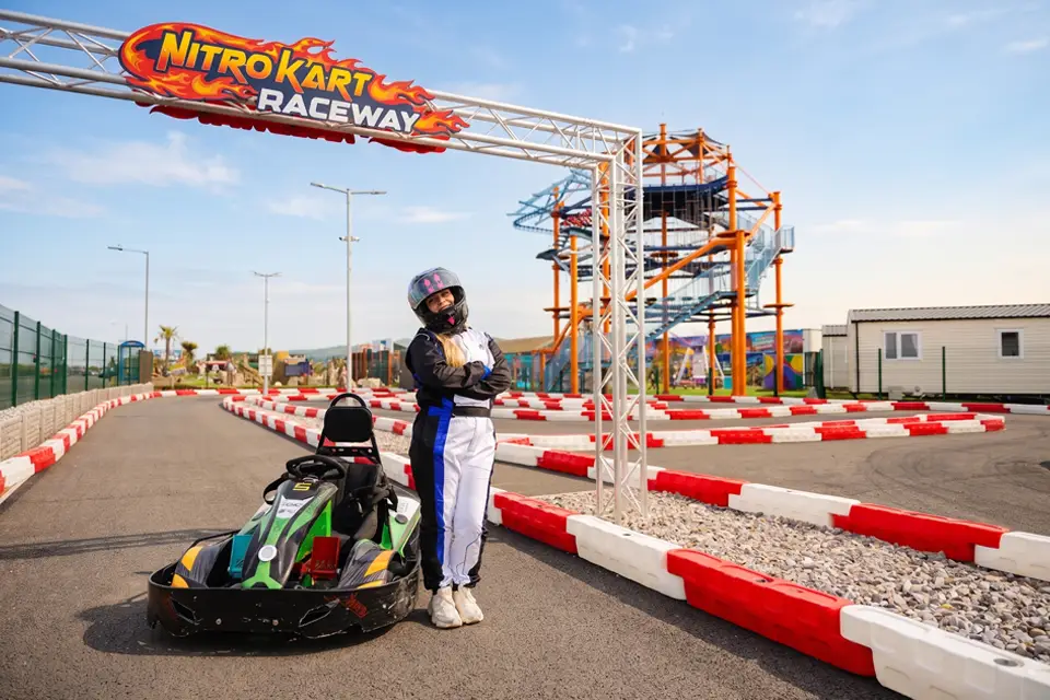 Girl standing in go kart uniform infront of track and high ropes